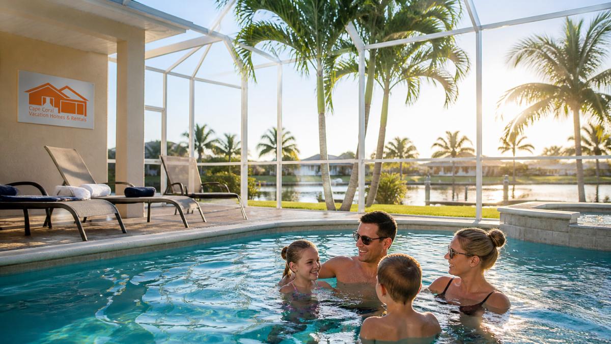 Family relaxing in a sunlit saltwater pool at one of our Cape Coral villa rentals with poolside lounge chairs.